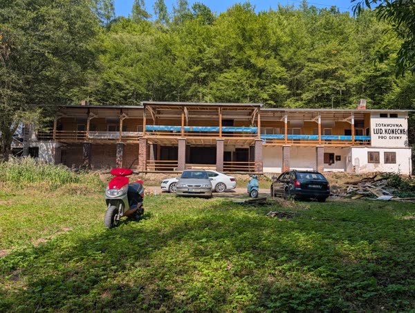 Celkový pohled na objekt zepředu — 42 m délky, zděné přízemí s podloubím, dřevěné patro s pavlačí, za tím les